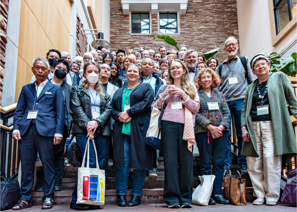 About fifty smiling humans filling an indoor staircase, wearing badges, some masked.